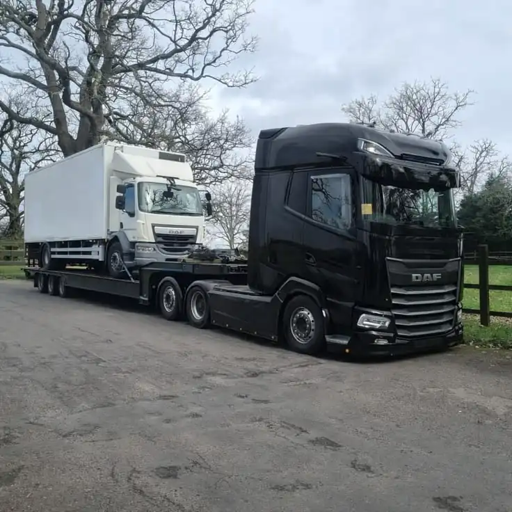 Vehicle carried on a low-loader trailer behind a black lorry